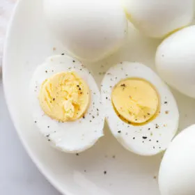 hard boiled eggs cut in half and displayed on a white plate with other whole hard boiled eggs. sprinkled with salt and pepper.