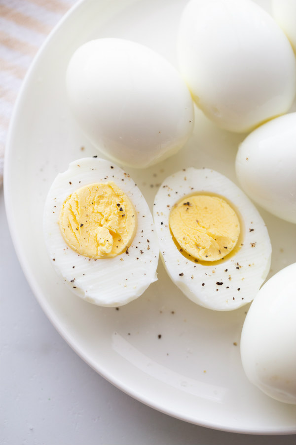 hard boiled eggs cut in half and displayed on a white plate with other whole hard boiled eggs. sprinkled with salt and pepper.