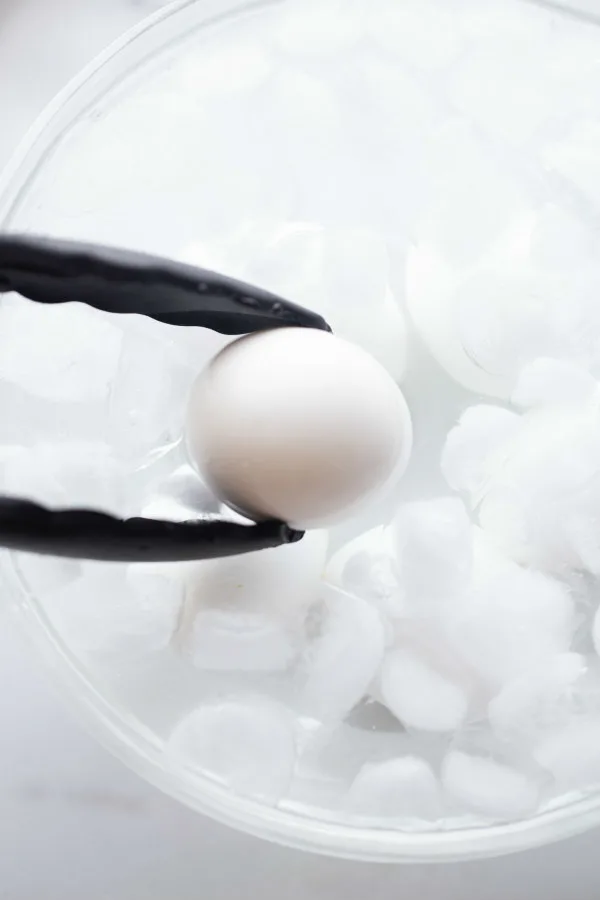 tongs placing a hard boiled egg into a bowl of ice water