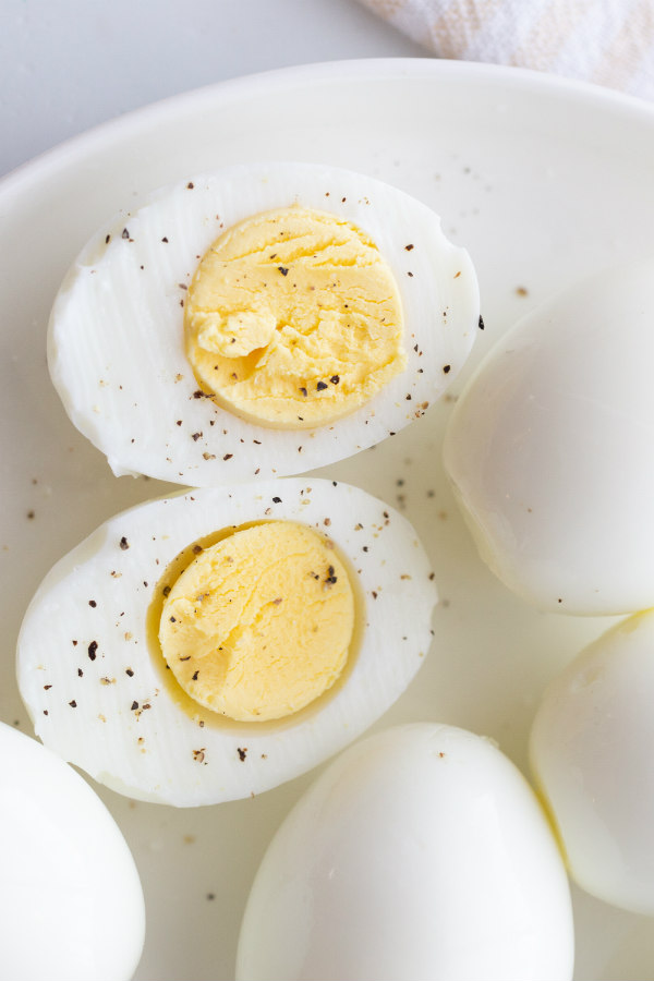 hard boiled eggs cut in half and displayed on a white plate with other whole hard boiled eggs. sprinkled with salt and pepper.