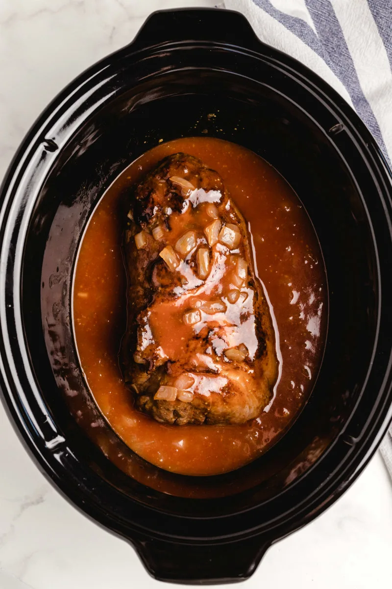 seared pork in a slow cooker with sauce ready to be cooked