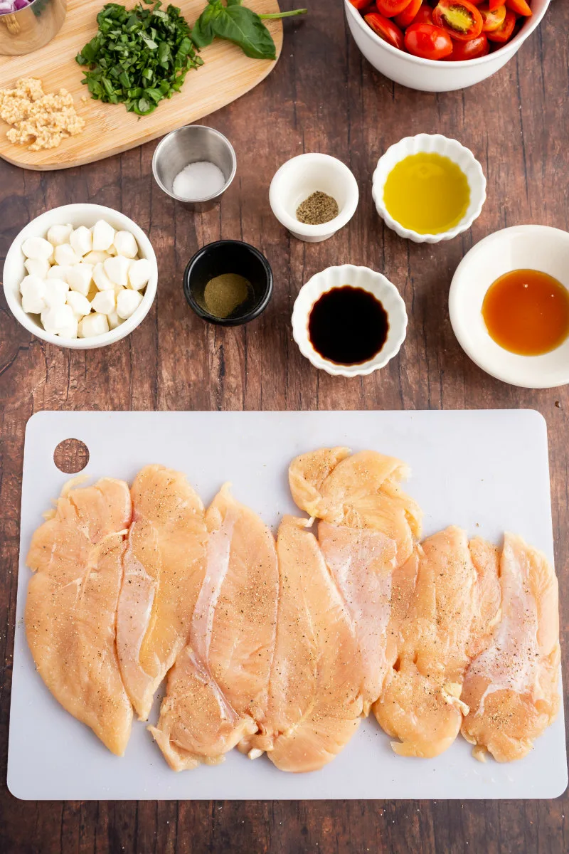 pounded out chicken on cutting board and more ingredients displayed for caprese chicken