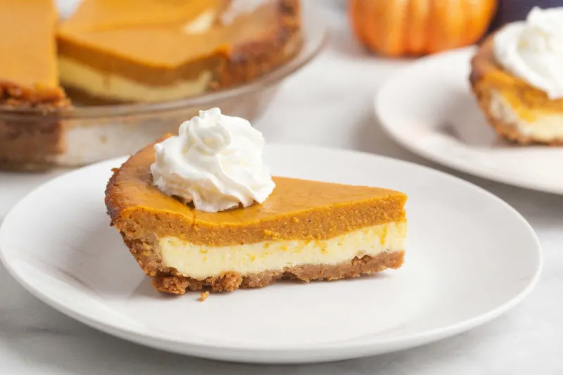 slice of pumpkin cream cheese pie with whipped cream on white plate