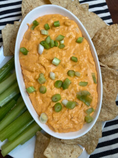 buffalo chicken dip in white bowl surrounded by celery and chips