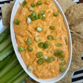 buffalo chicken dip in white bowl surrounded by celery and chips