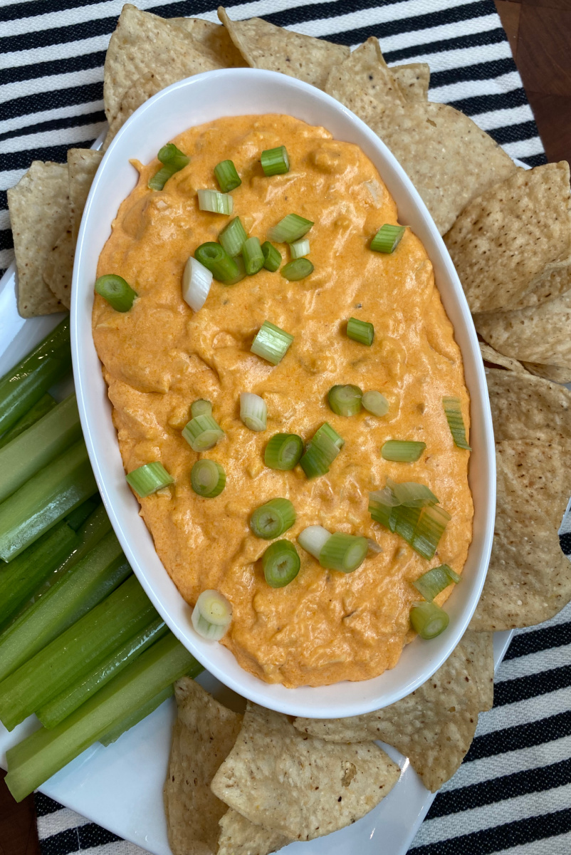 buffalo chicken dip in white bowl surrounded by celery and chips