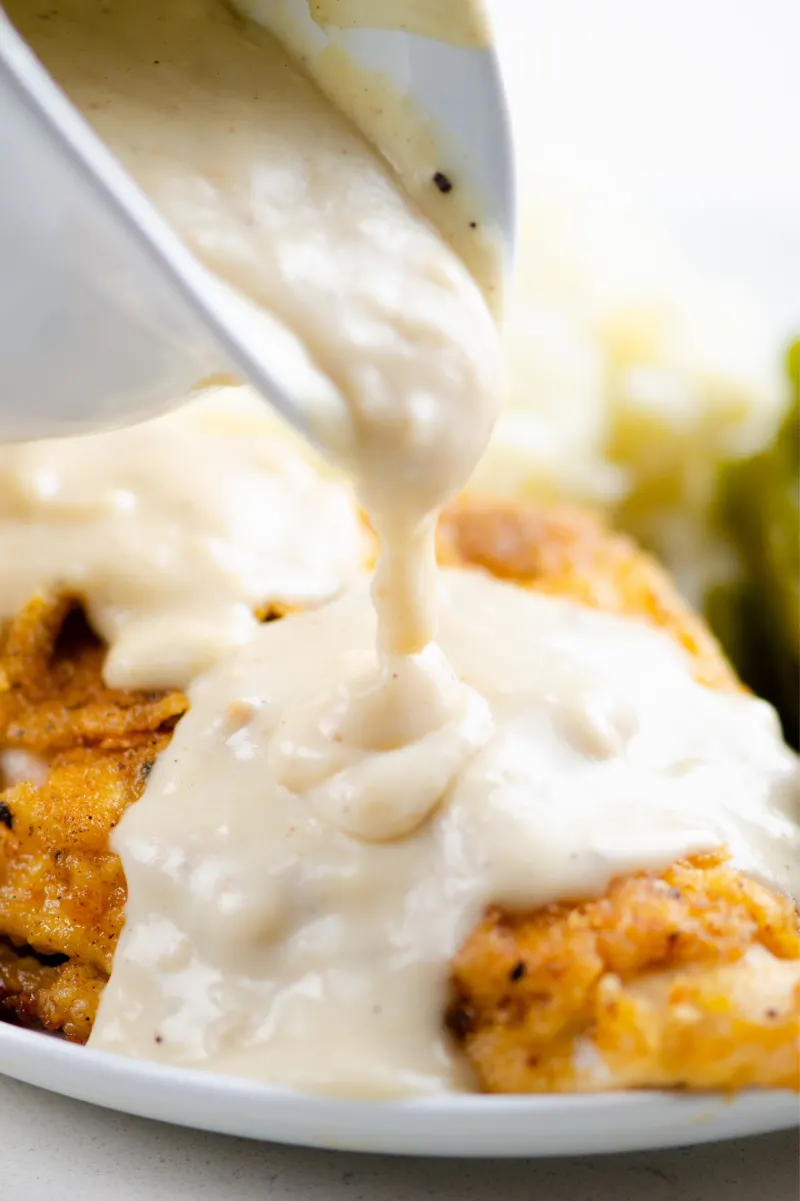 pouring country gravy over fried chicken