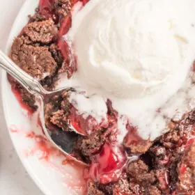 chocolate cherry dump cake with ice cream and spoon on white plate