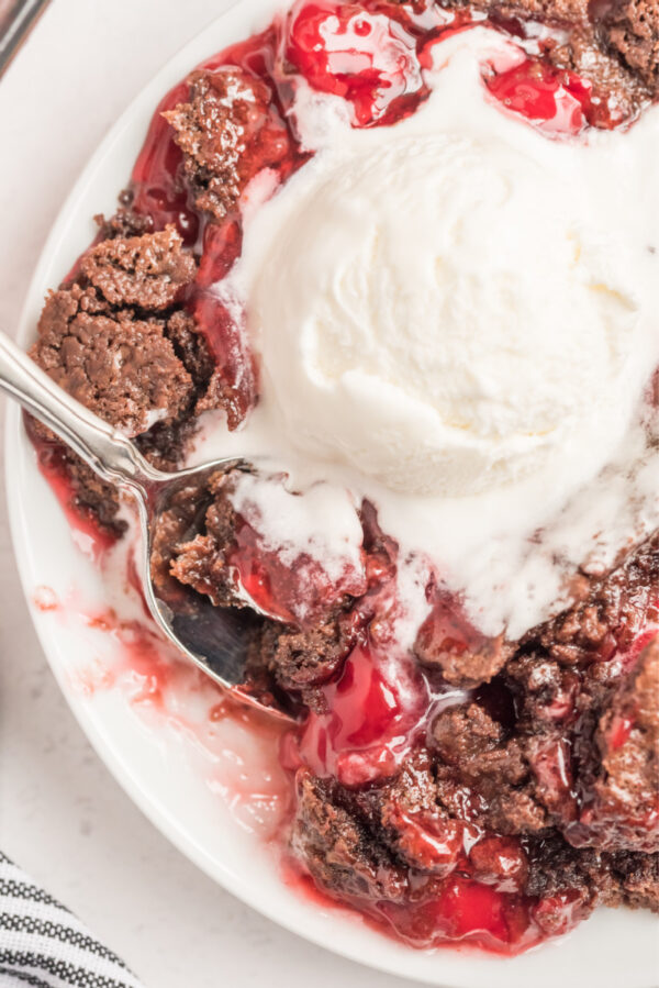 chocolate cherry dump cake with ice cream and spoon on white plate