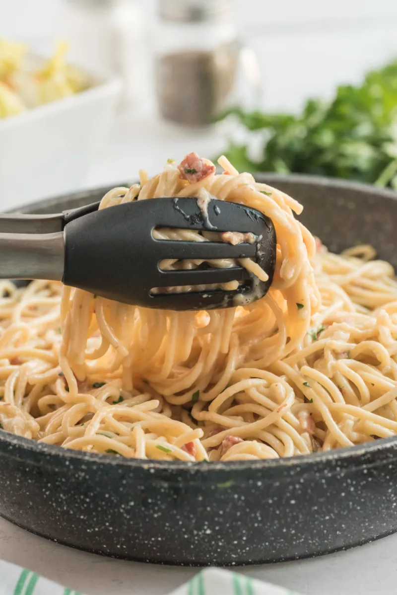 tongs taking spaghetti carbonara out of pan