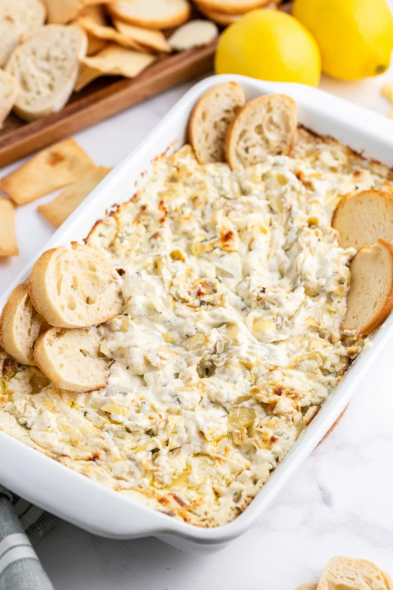 casserole dish with cheesy lemon rosemary artichoke dip and baguette