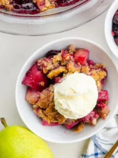 pear and berry crisp in a white bowl with vanilla ice cream