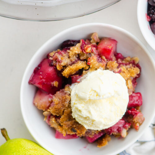 pear and berry crisp in a white bowl with vanilla ice cream