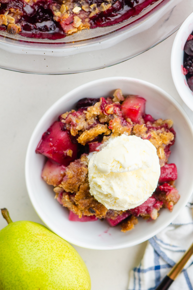 pear and berry crisp in a white bowl with vanilla ice cream