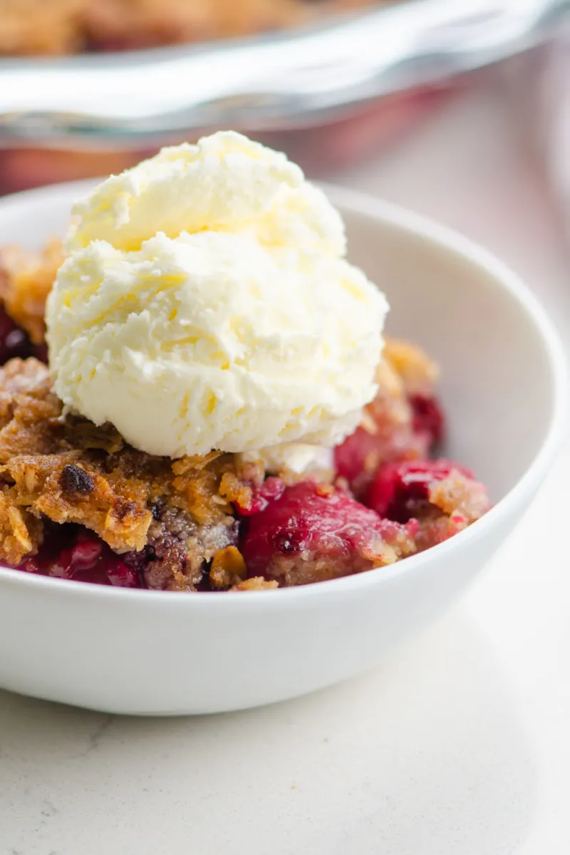 pear and berry crisp in a white bowl with ice cream
