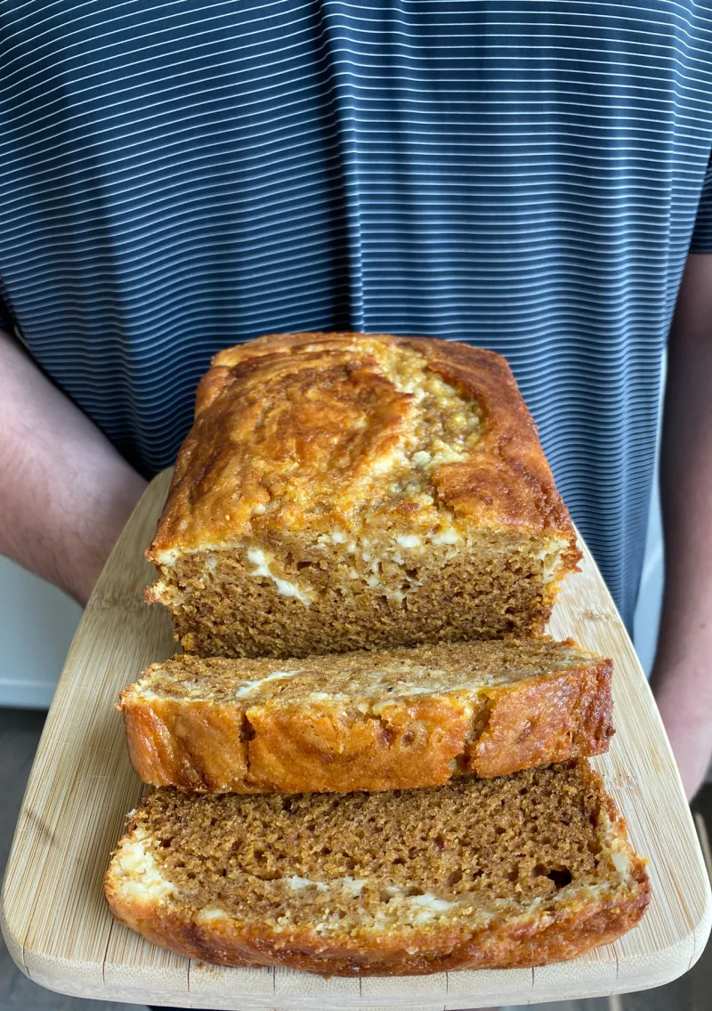 loaf of pumpkin cheesecake bread sliced on bread board