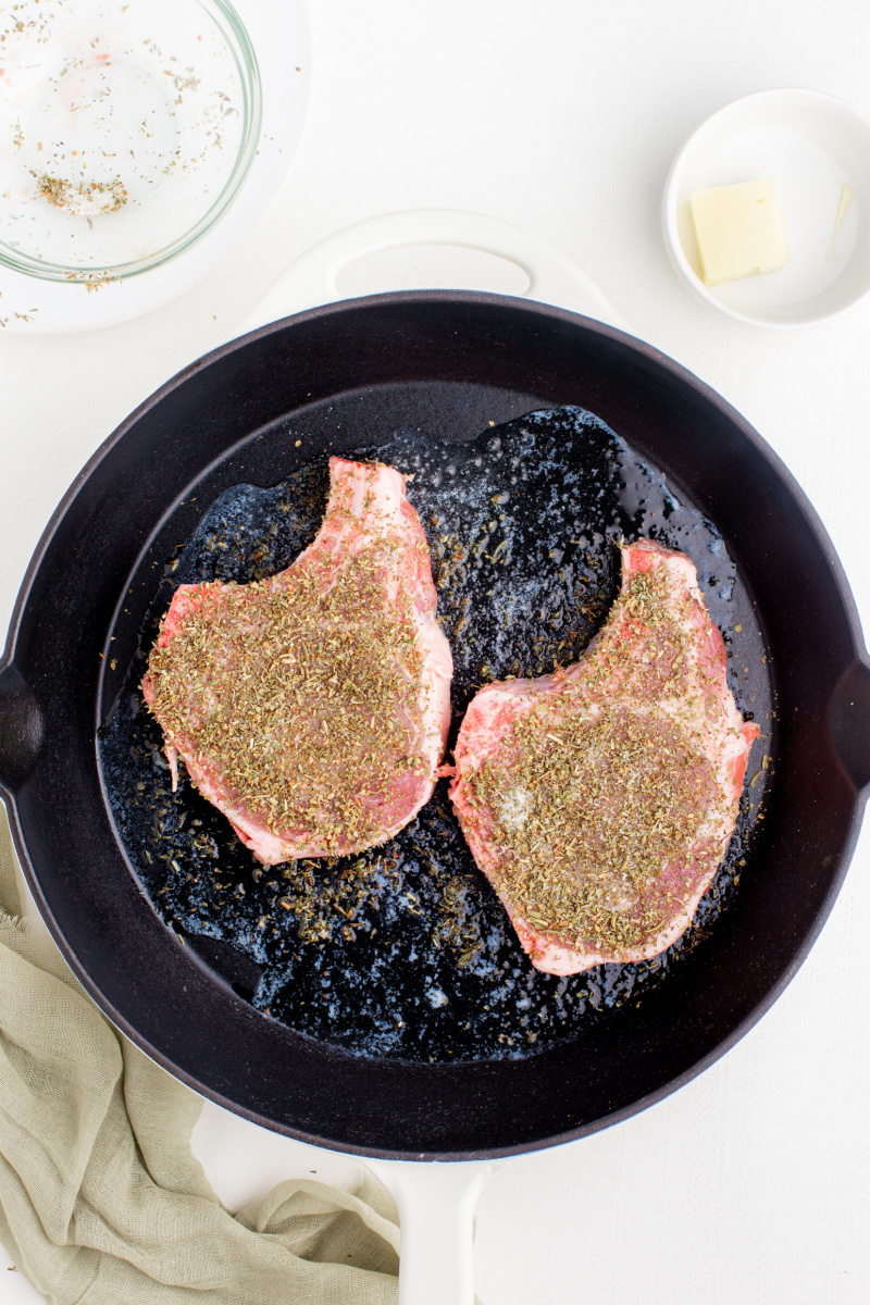 two pork chops with seasoning in black skillet