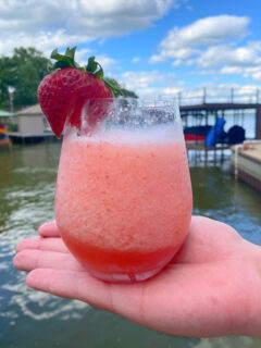 hand holding a glass of strawberry frose with lake in background