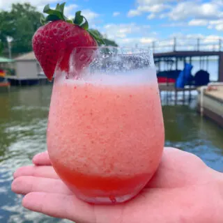 hand holding a glass of strawberry frose with lake in background