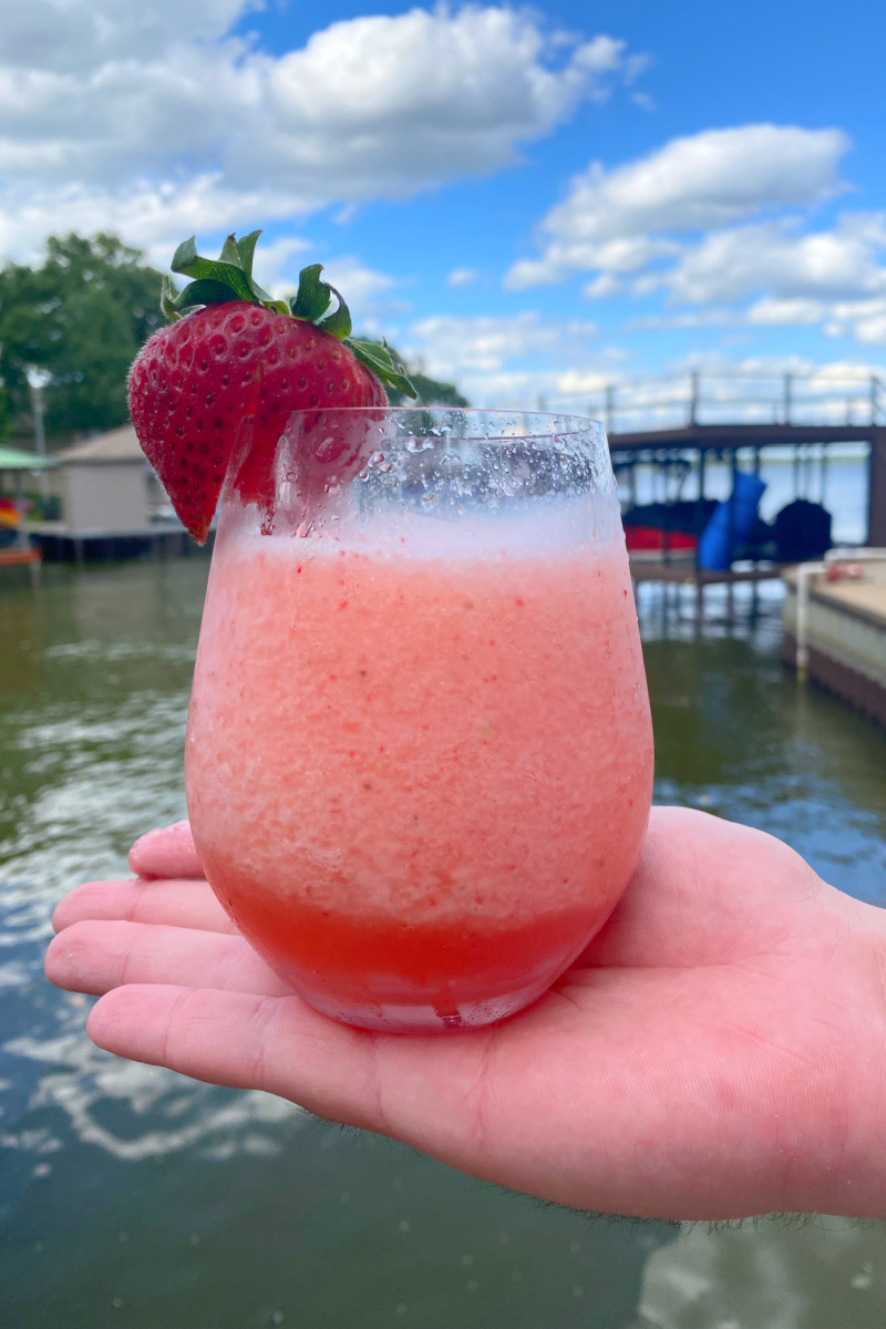 hand holding a glass of strawberry frose with lake in background