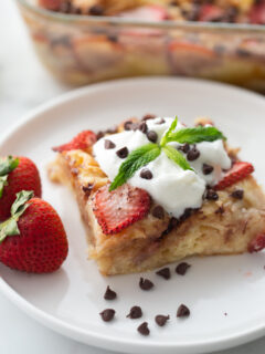 slice of strawberry chocolate chip croissant pudding on plate topped with whipped cream