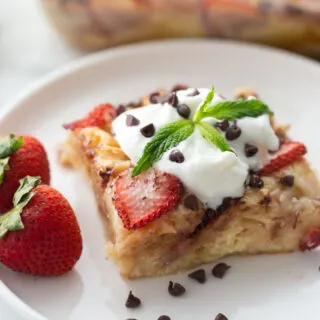 slice of strawberry chocolate chip croissant pudding on plate topped with whipped cream
