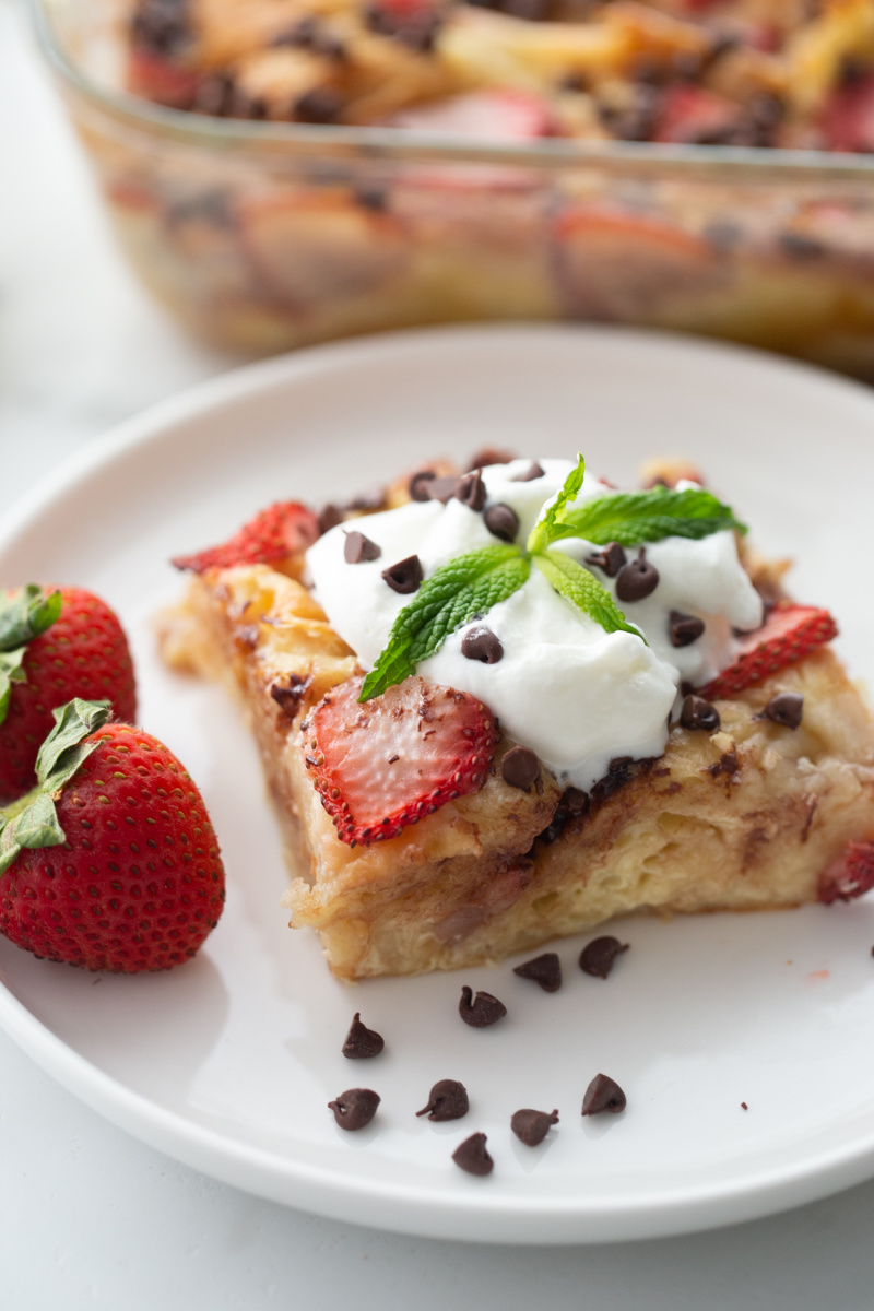 slice of strawberry chocolate chip croissant pudding on plate topped with whipped cream