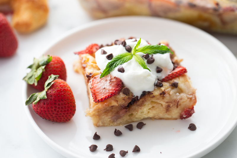 slice of strawberry chocolate chip croissant pudding on plate topped with whipped cream