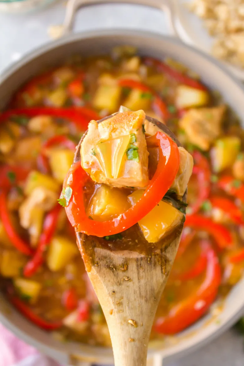 wooden spoon with chicken stir fry on it pan underneath