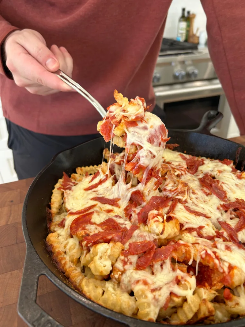 fork pulling fries and cheese from pizza fries skillet