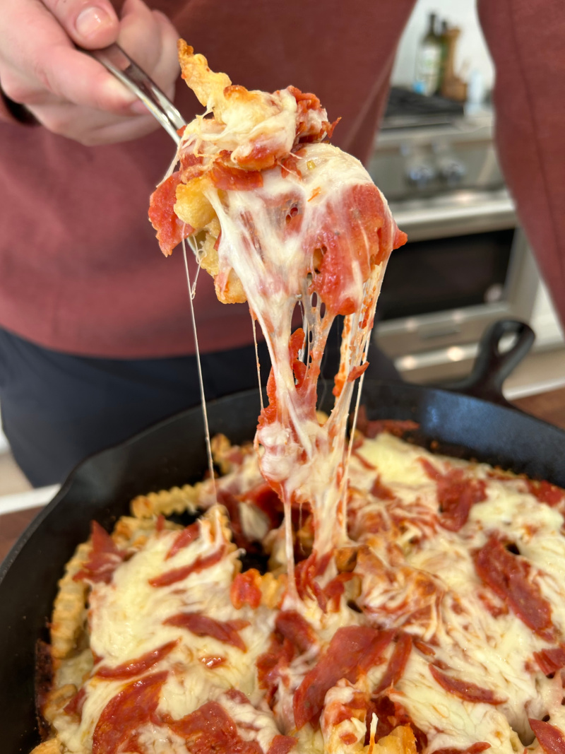 fork pulling up fries and cheese from skillet