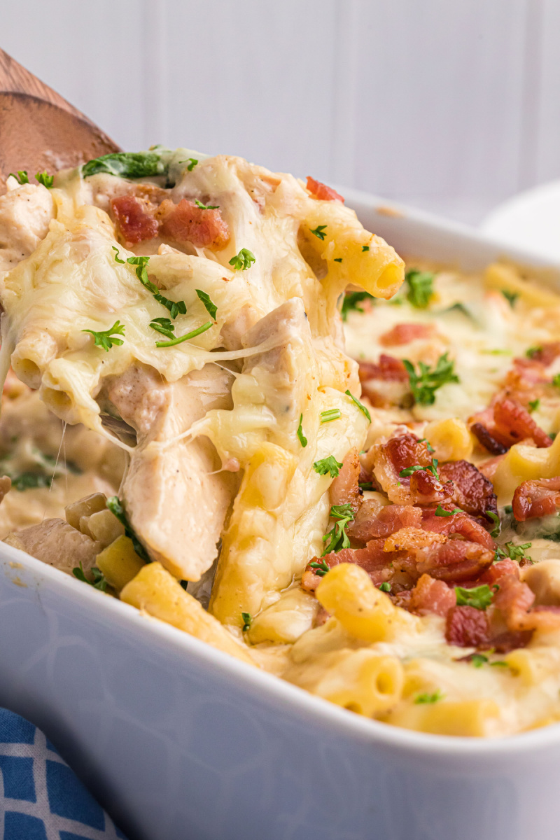 spooning creamy tuscan chicken pasta bake out of casserole dish
