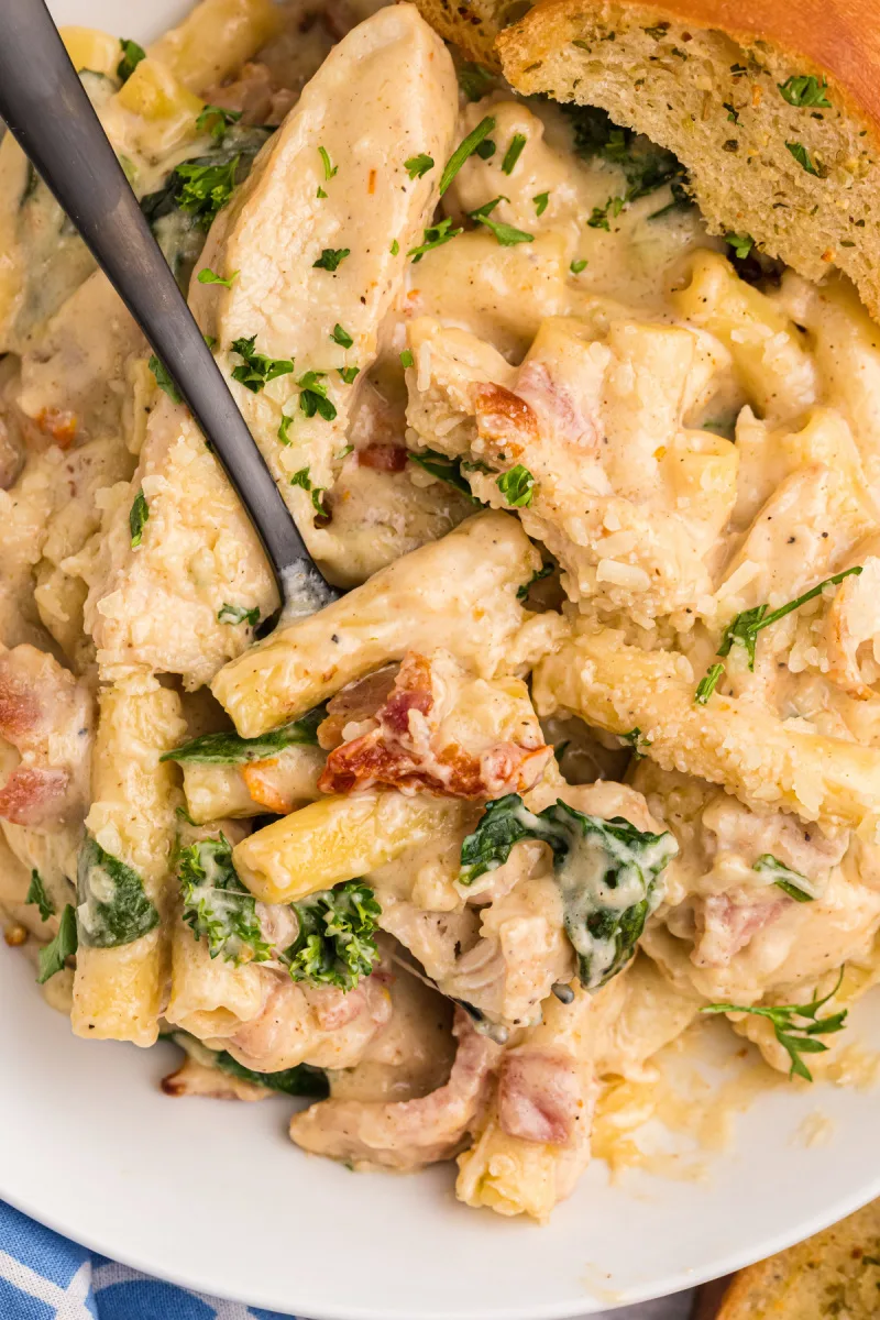 spooning out creamy tuscan chicken pasta bake off plate