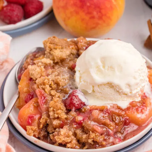 raspberry peach crumble in a dish with vanilla ice cream on top