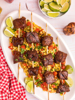 grilled beef kabobs over corn tomato salad on platter