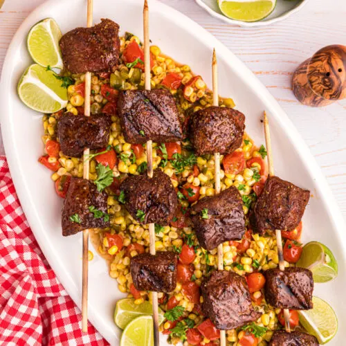 grilled beef kabobs over corn tomato salad on platter