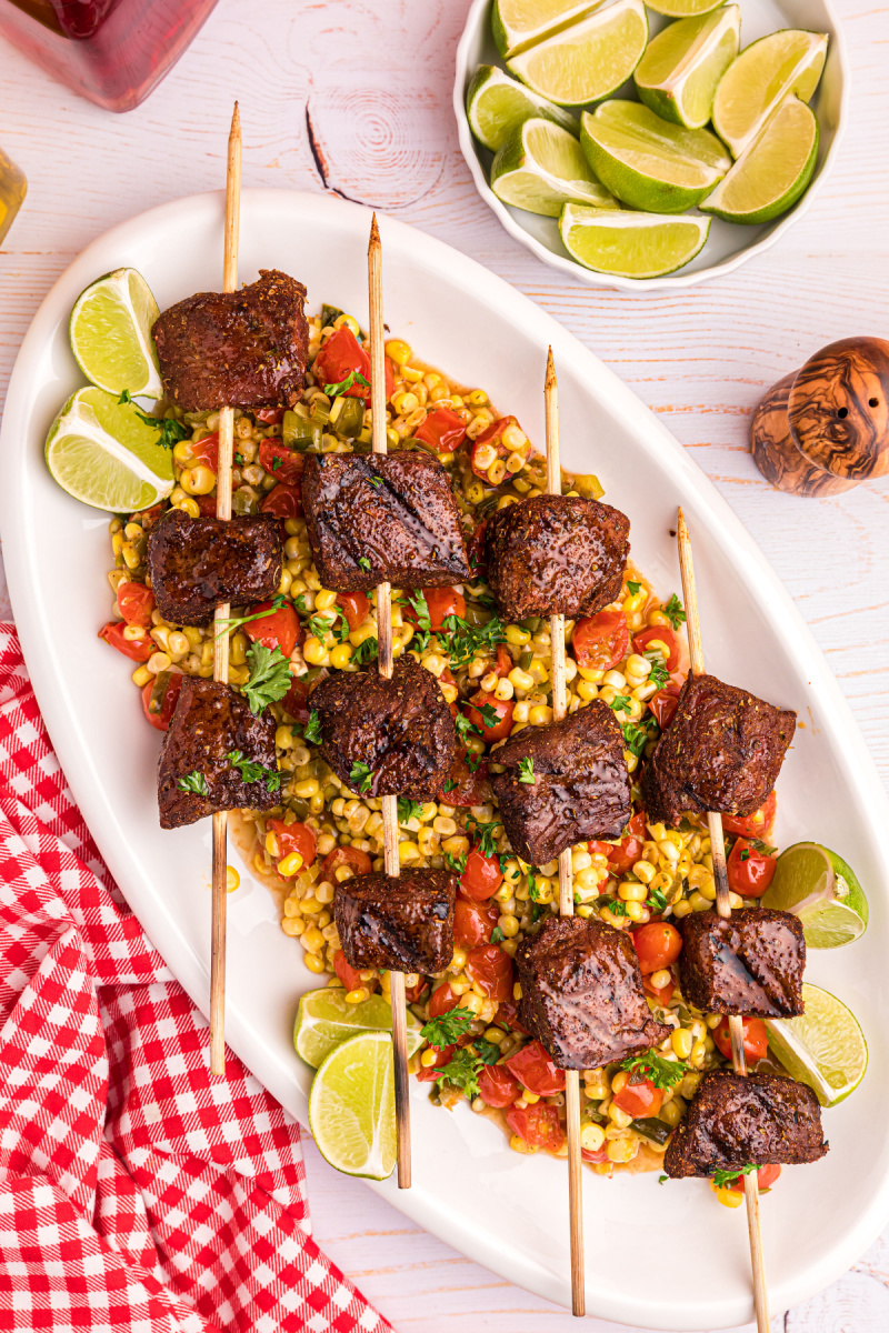 grilled beef kabobs over corn tomato salad on platter