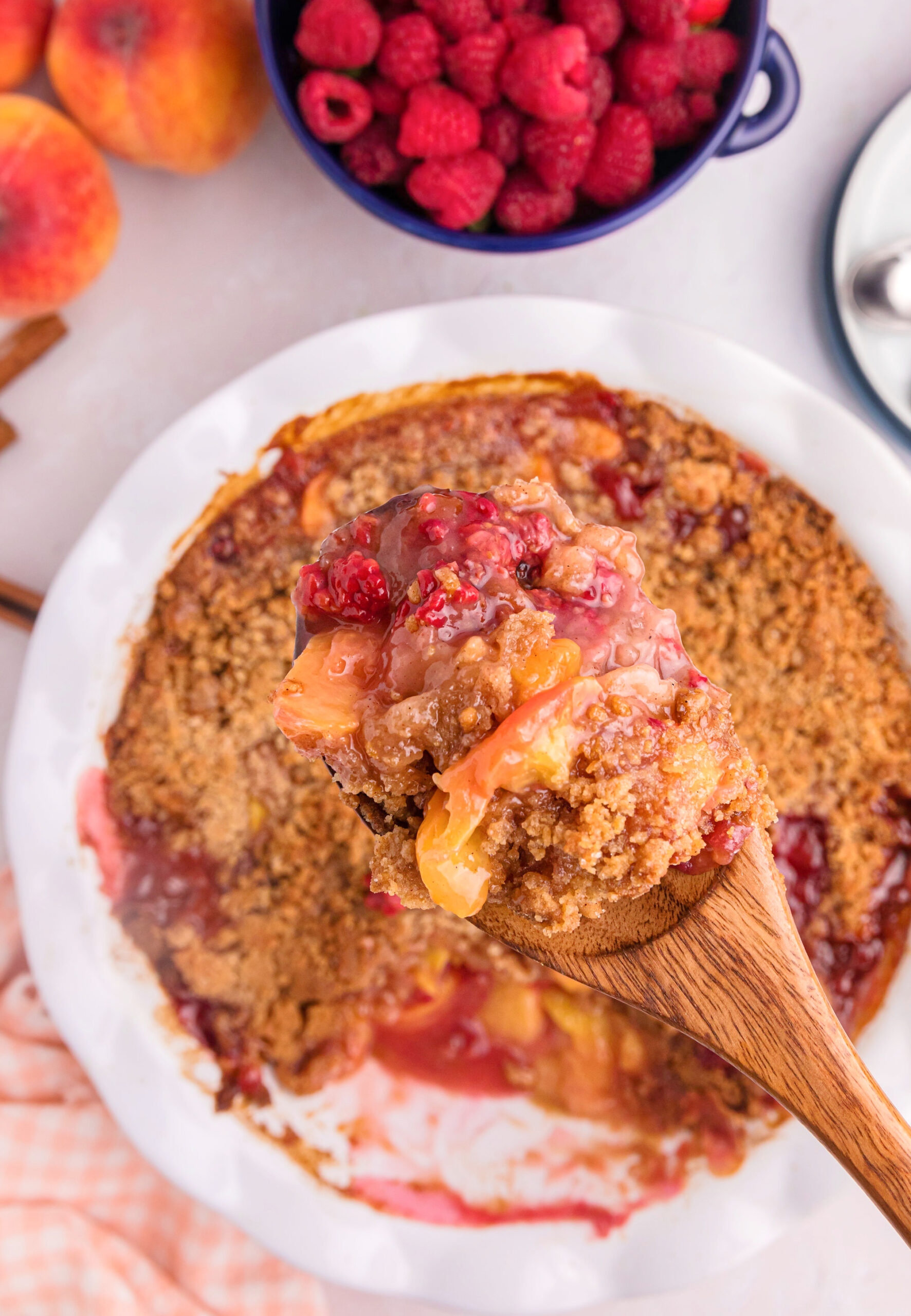 raspberry peach crumble in dish with wooden spoonful of it above