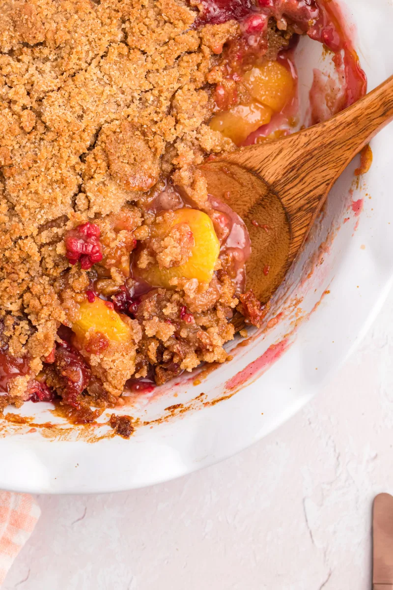 peek at raspberry peach crumble in dish with wooden spoon