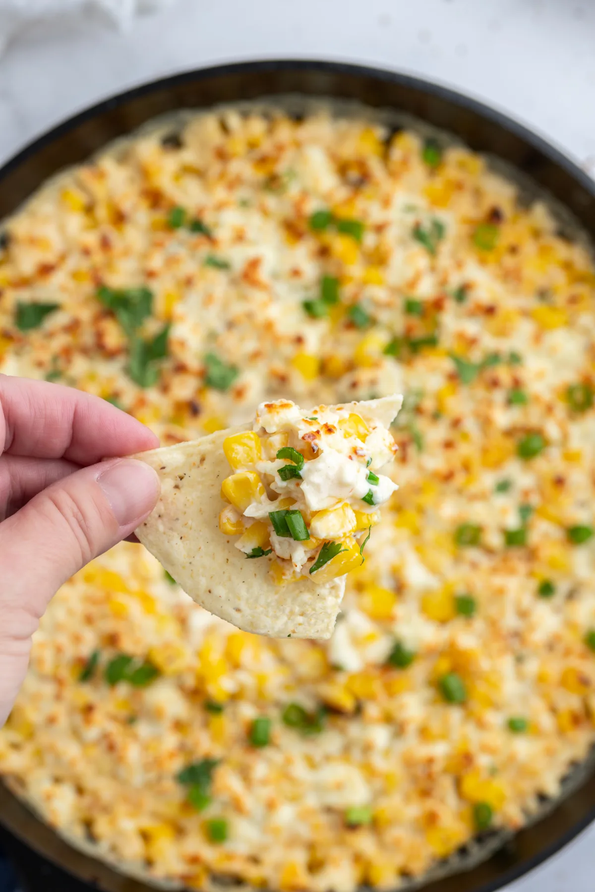 hand holding chip with baked elote dip