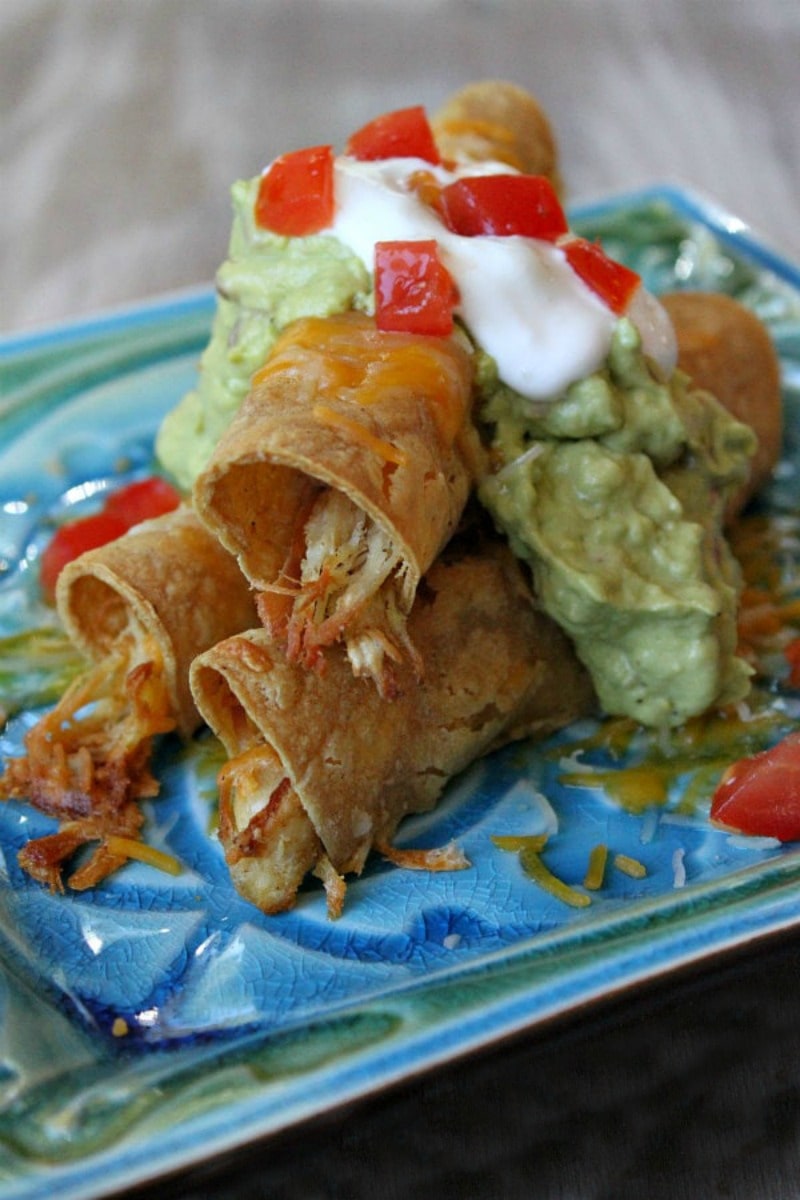 Baked Chicken Taquitos stacked on plate with garnishes