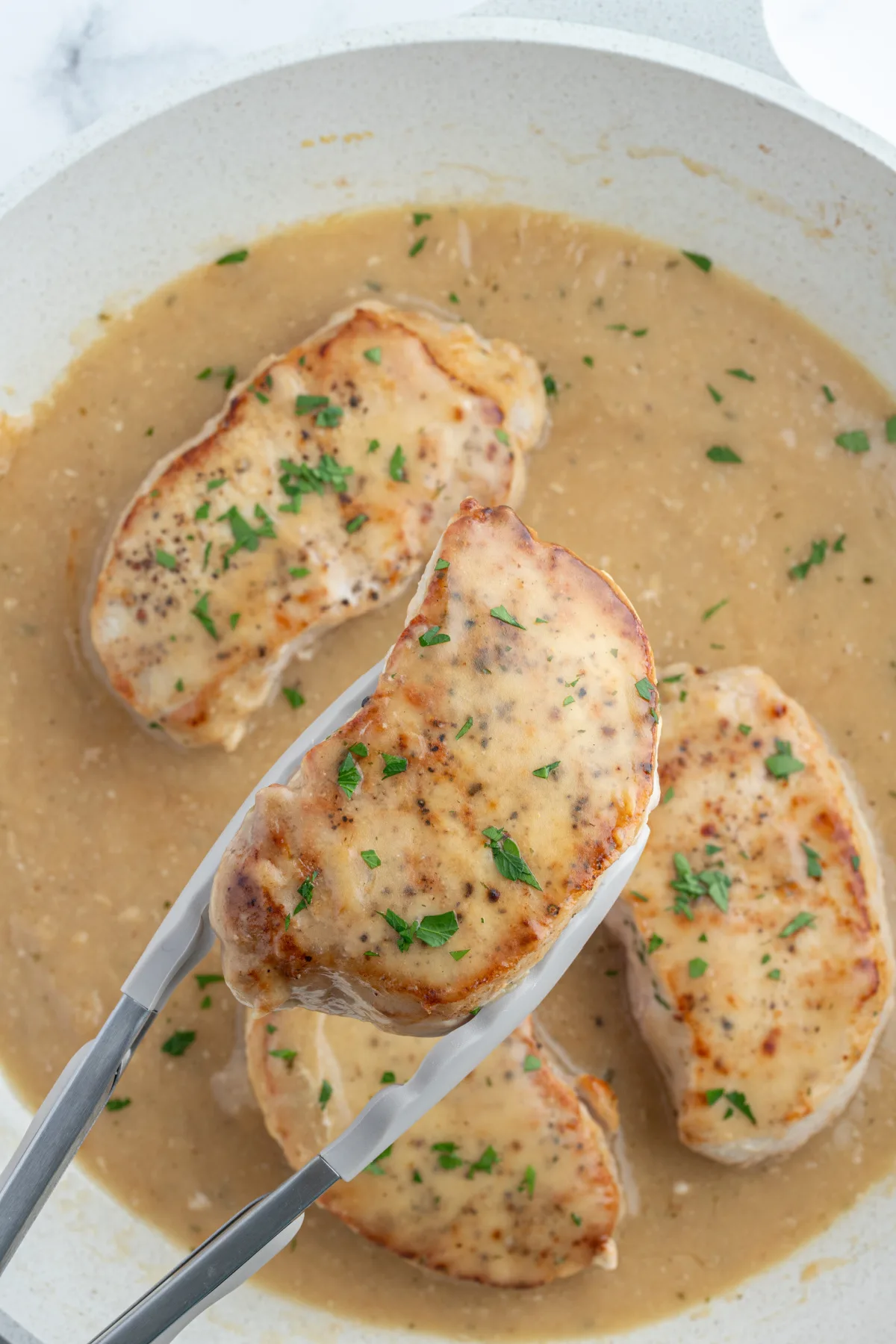 tongs taking ranch pork chop out of pan