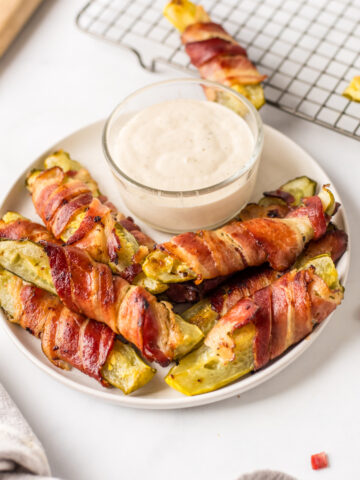 bacon wrapped dill pickles displayed around bowl of ranch dressing