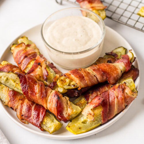 bacon wrapped dill pickles displayed around bowl of ranch dressing