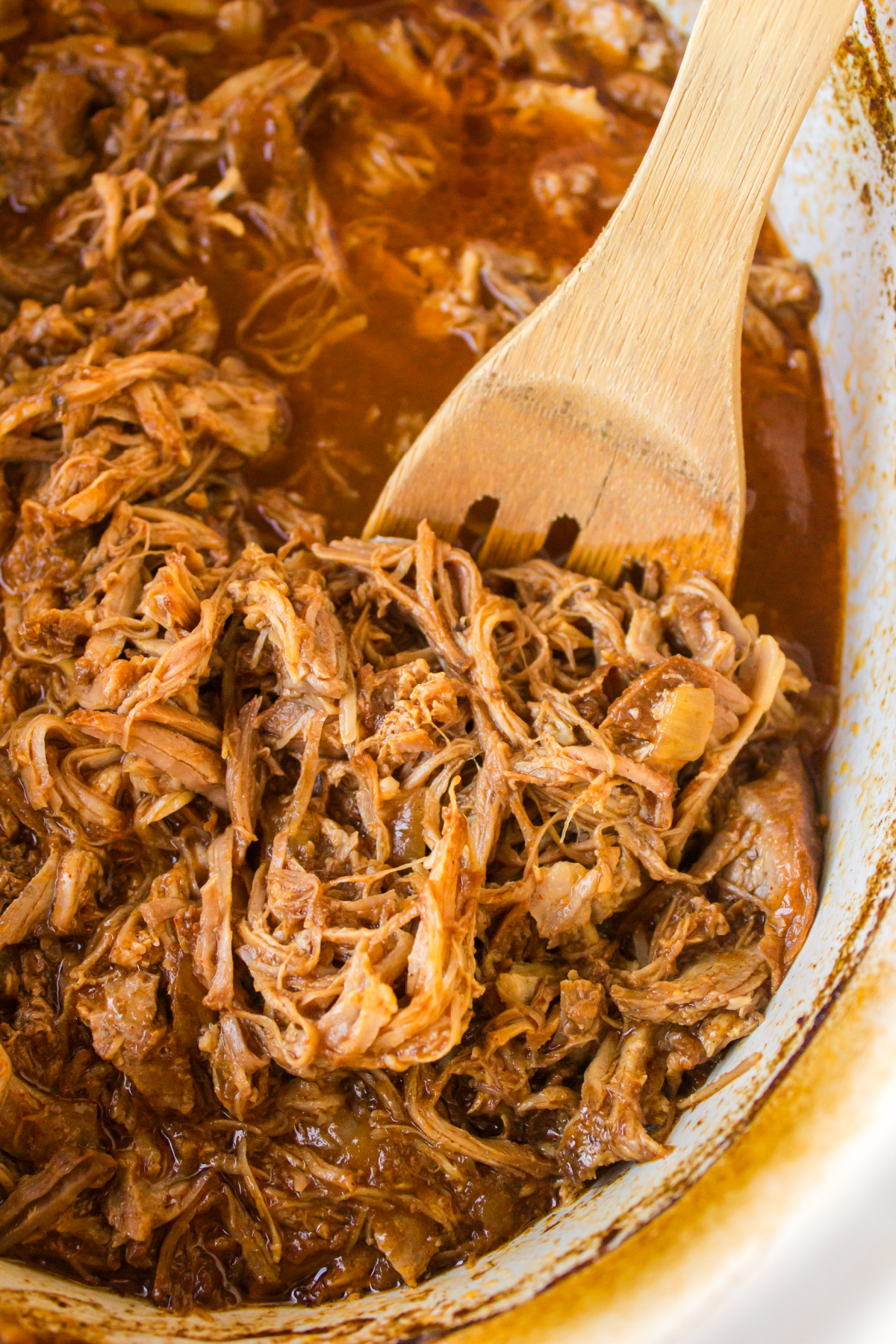 slow cooker texas pulled pork in slow cooker with wooden spoon