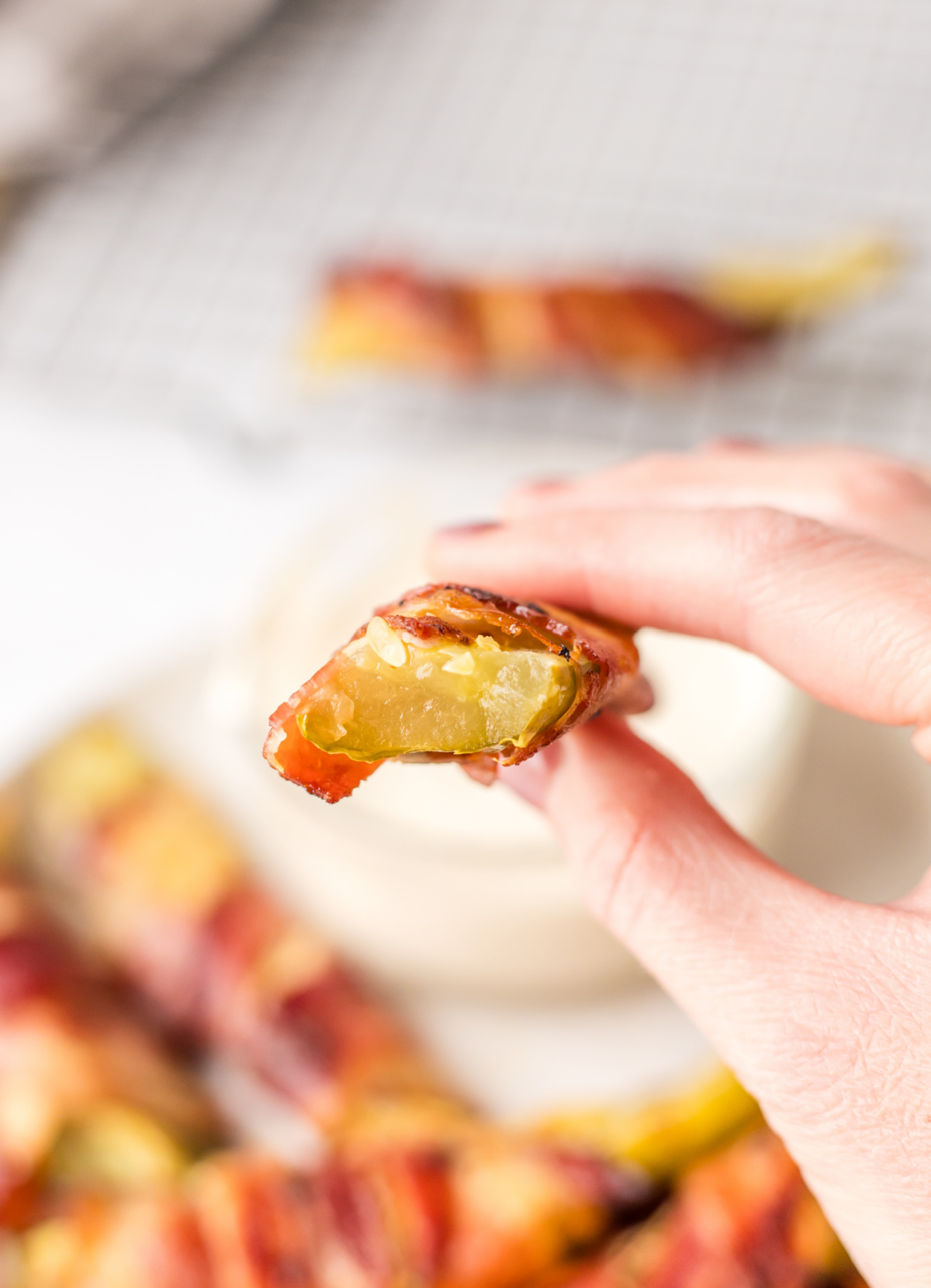 hand holding bacon wrapped dill pickle with bite taken out of it