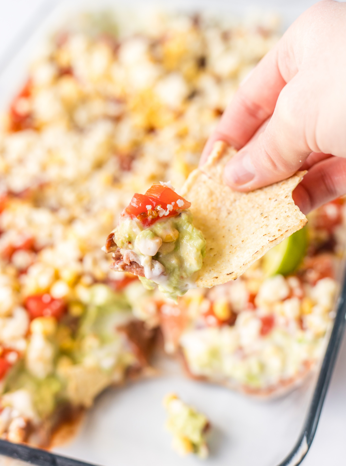 7 Layer Mexican Dip recipe from RecipeBoy.com hand holding chip over 7 layer mexican dip recipe