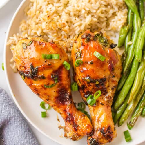 two honey chicken drumsticks on a plate with rice and green beans