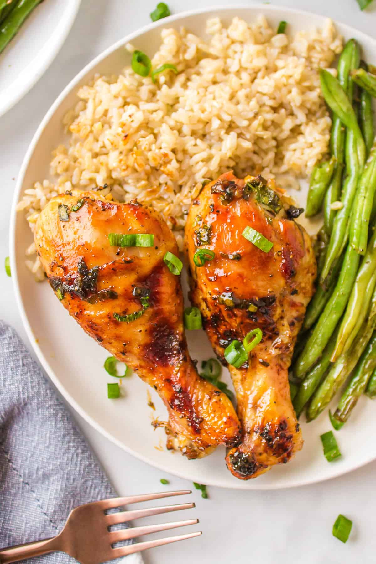 This Honey Chicken Drumsticks recipe is an easy, family friendly dinner recipe, and you will only need 5 ingredients to make it. two honey chicken drumsticks on a plate with rice and green beans