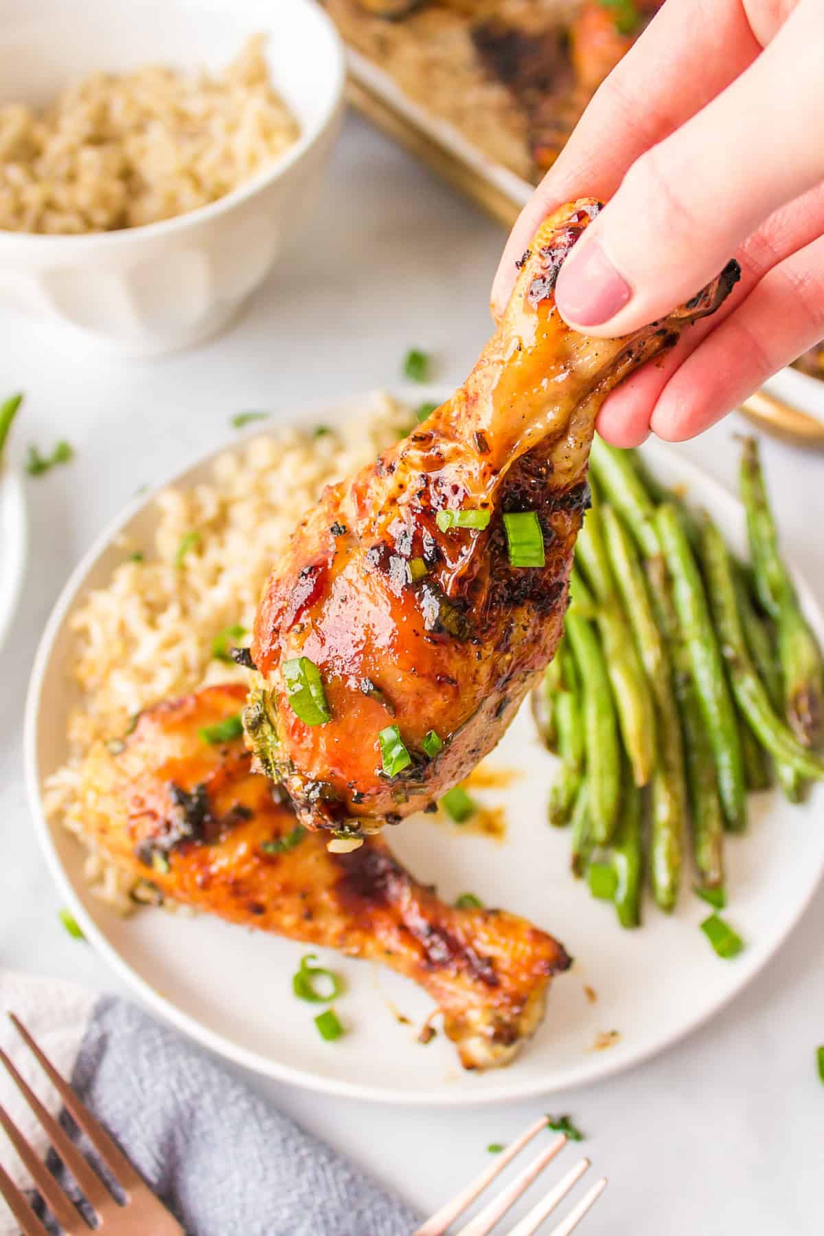 This Honey Chicken Drumsticks recipe is an easy, family friendly dinner recipe, and you will only need 5 ingredients to make it. hand picking up a honey chicken drumstick off plate